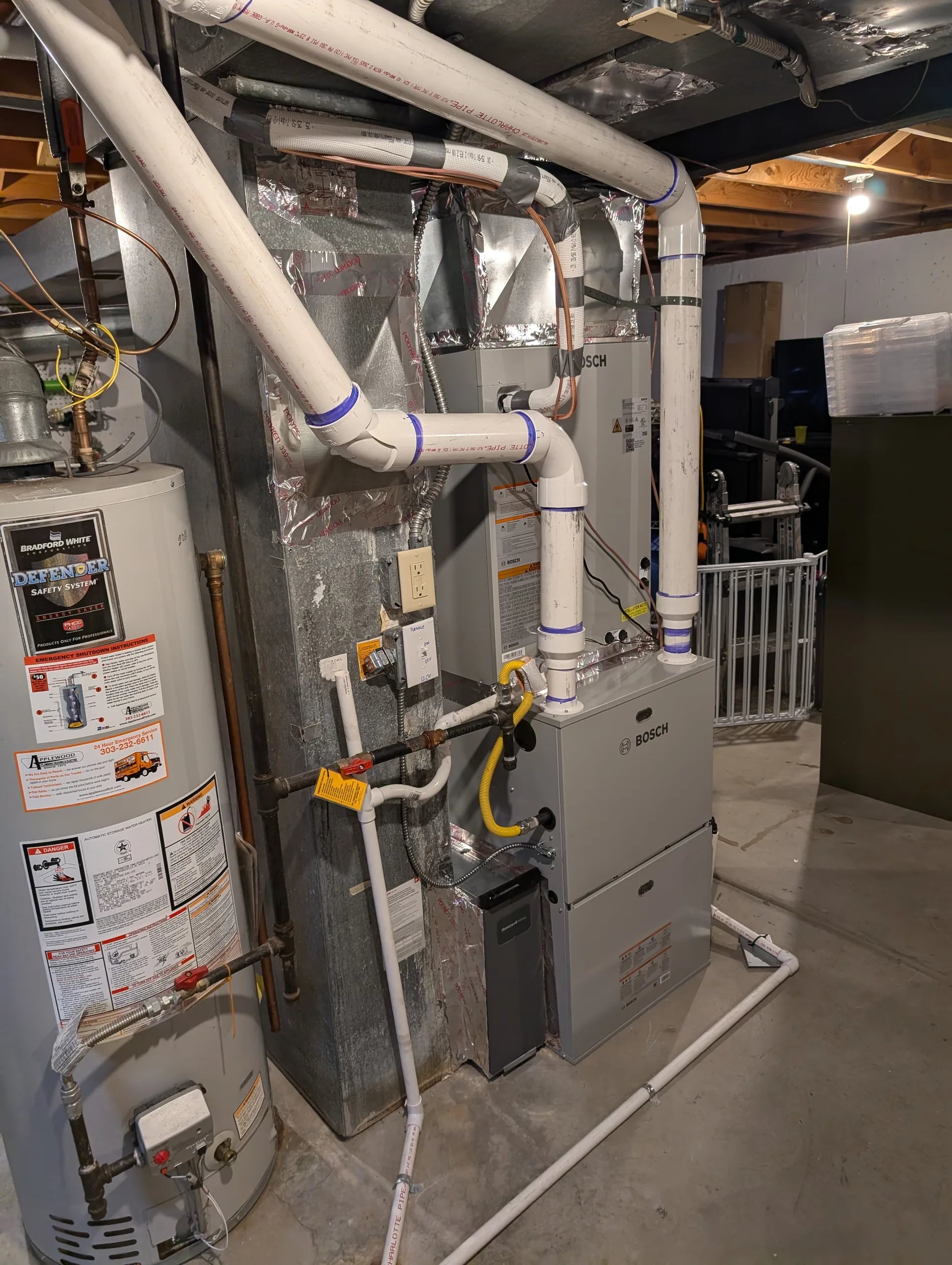 A Bosch furnace next to a gas water heater with white PVC venting in a basement