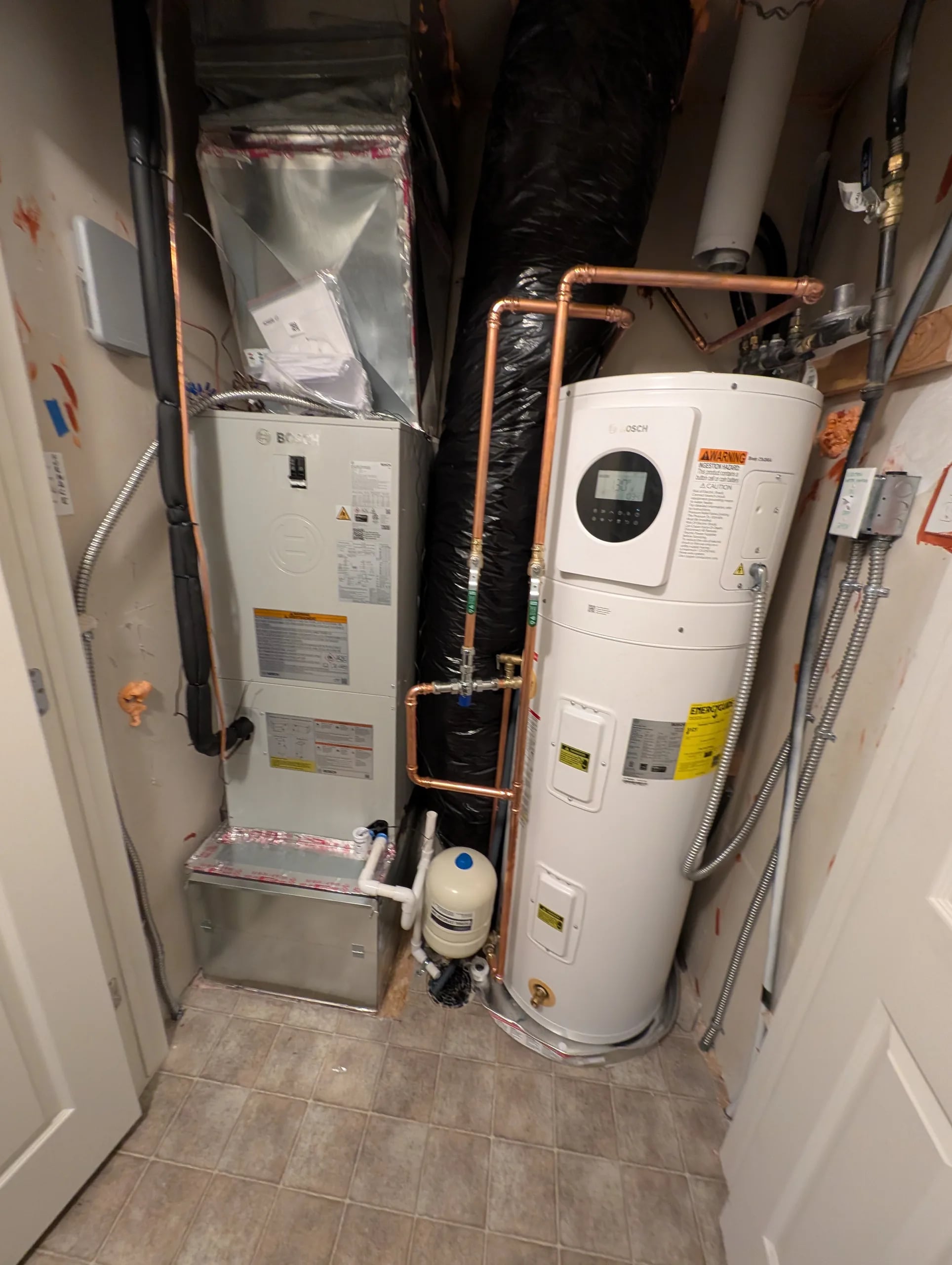 Bosch air handler beside a heat pump water heater with copper and orange lines in a utility closet.